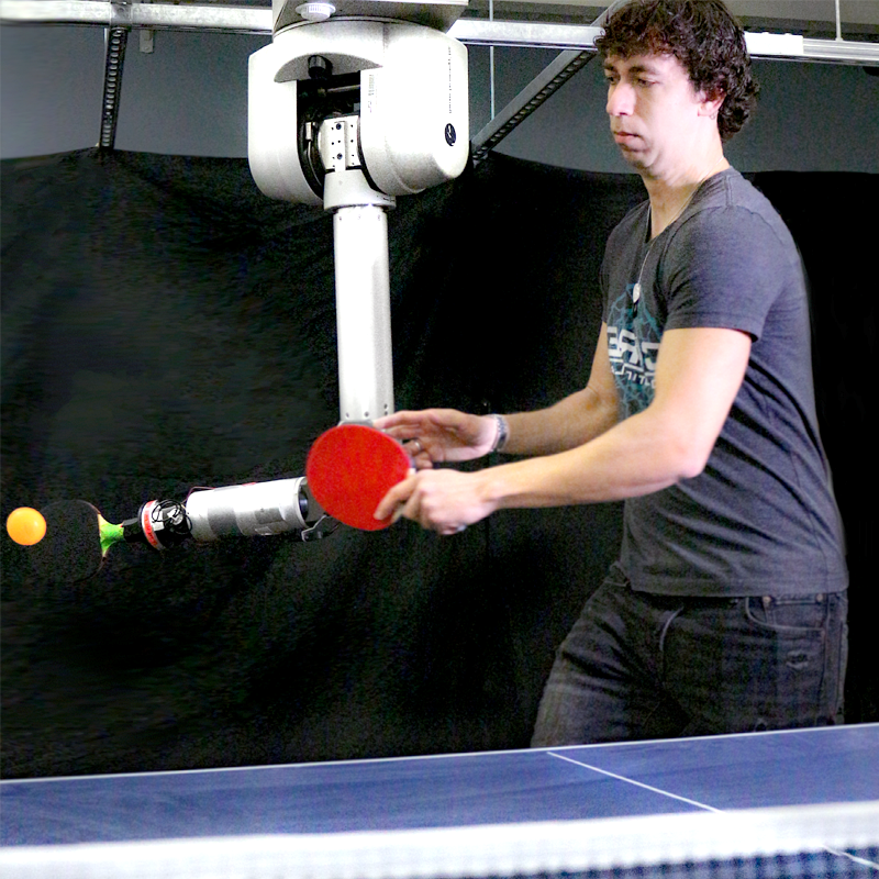 man holding a ping pong paddle and playing ping pong with a robotics arm