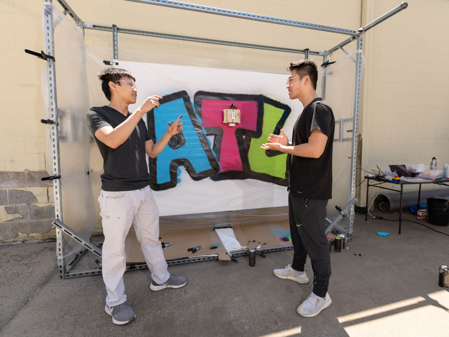two student standing infront of the graphitti art their robot created