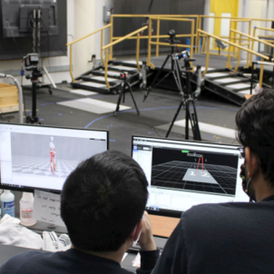 Two people behind a desk with monitors. They are looking over the monitors into an auditorium